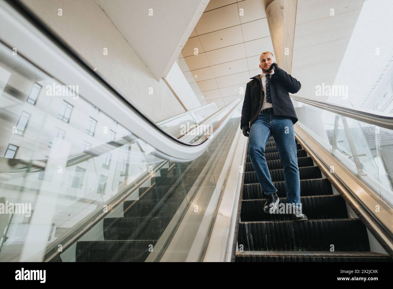 A businessman descends an escalator within a contemporary, airy corporate building, embodying efficiency and urban lifestyle. Stock Photo