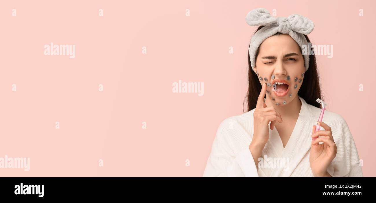 Displeased young woman with thumb tacks on face and razor against pink background with space for text. Depilation concept Stock Photo