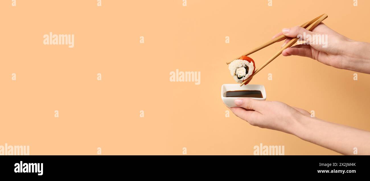 Female hands with tasty sushi roll, chopsticks and soy sauce on beige background with space for text Stock Photo