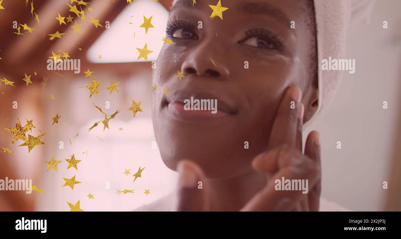 Image of gold stars floating over happy african american woman cleansing face in bathroom Stock Photo