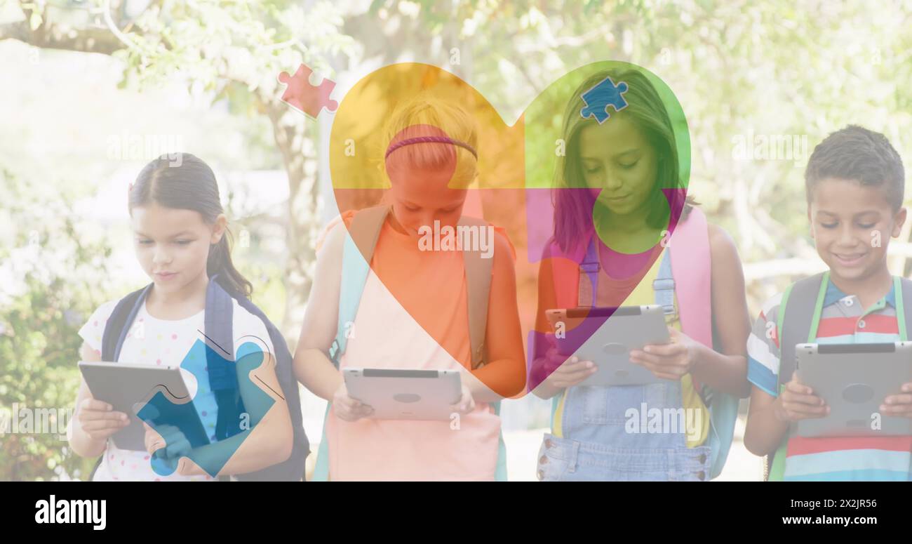 Image of colourful puzzle pieces heart over school children using tablets Stock Photo