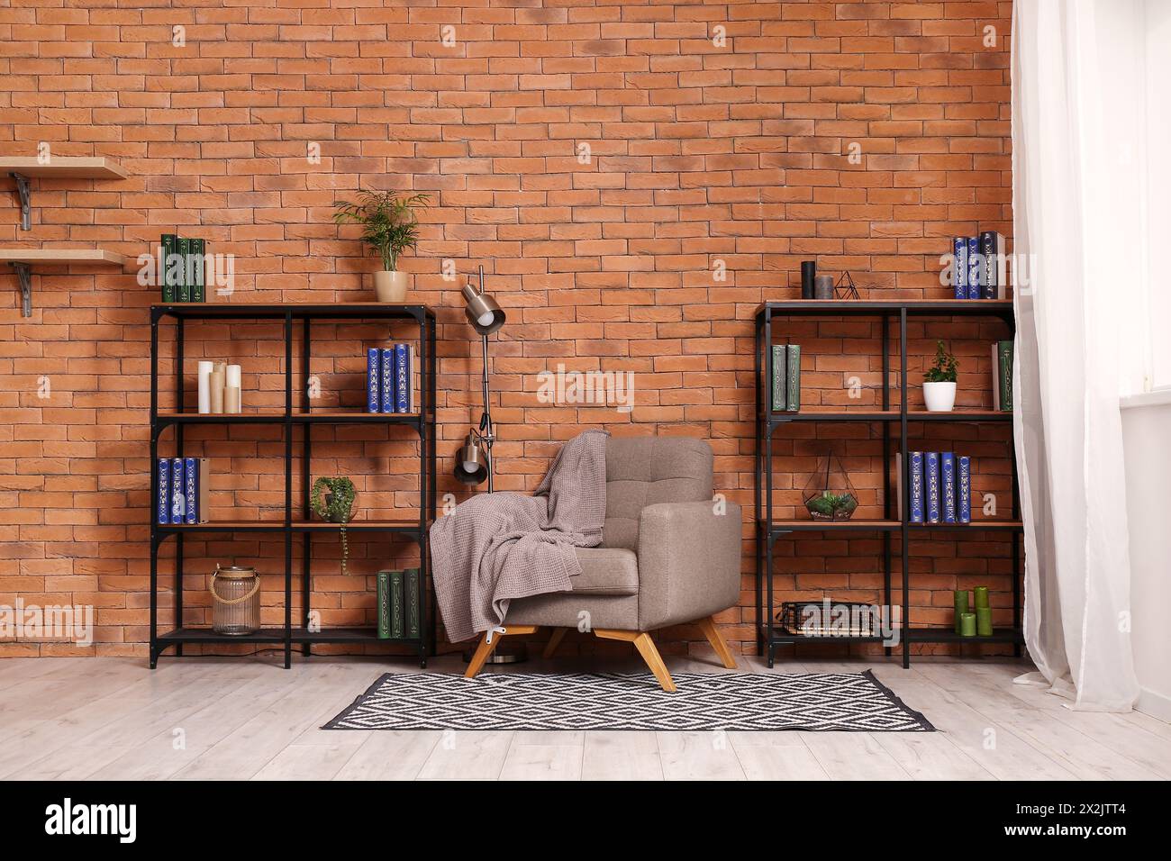 Shelving units, grey armchair and lamp near brown brick wall in living room Stock Photo