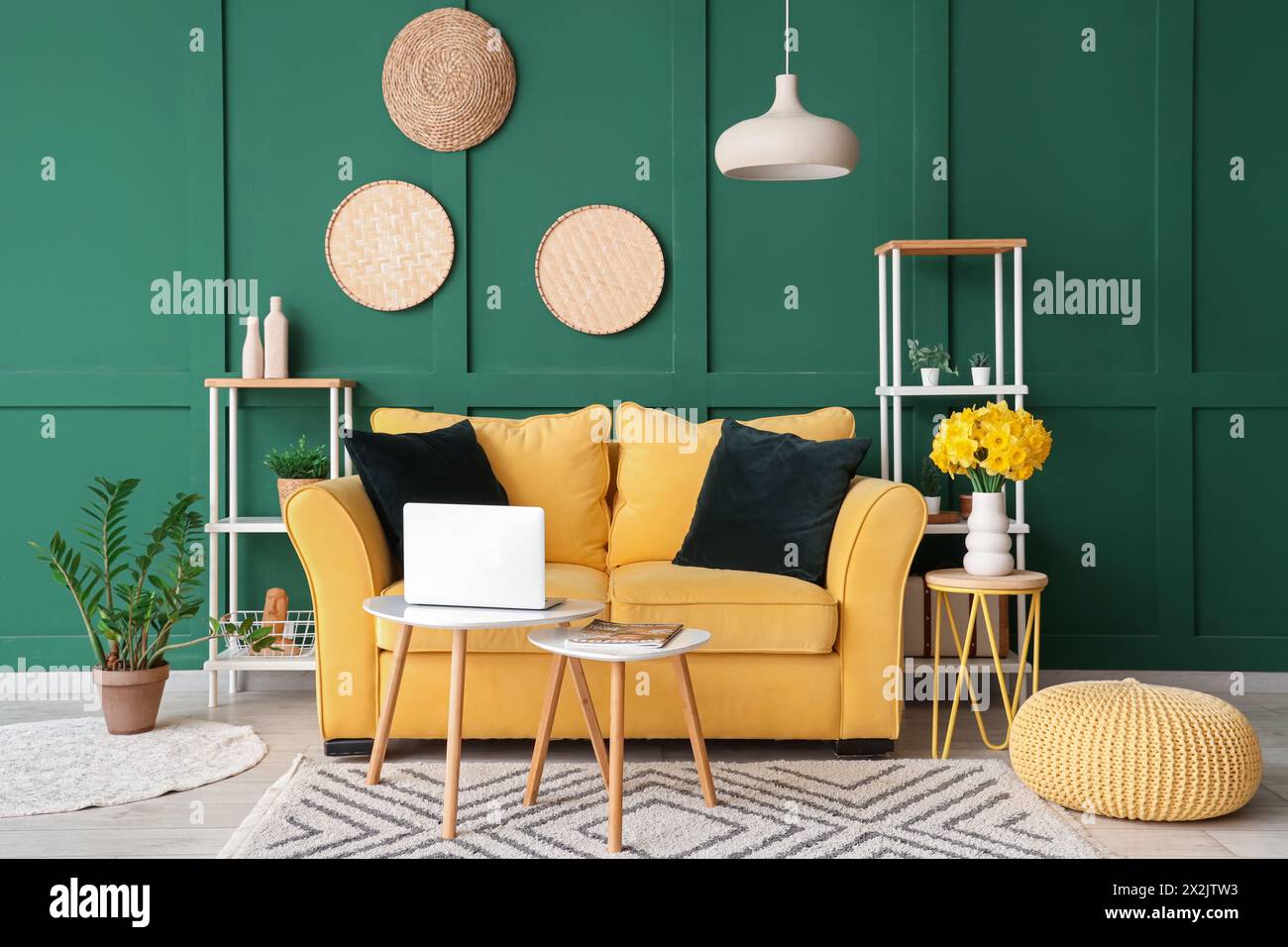Stylish interior of green living room with yellow sofa, coffee tables, laptop and bouquet of narcissus flowers Stock Photo