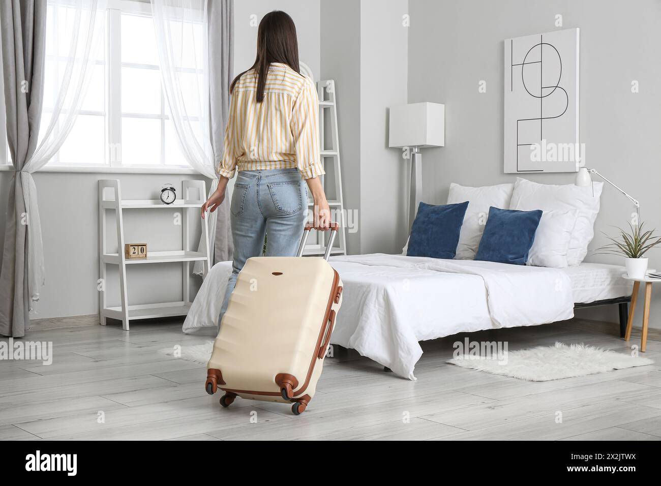 Woman with suitcase in light hotel room, back view Stock Photo