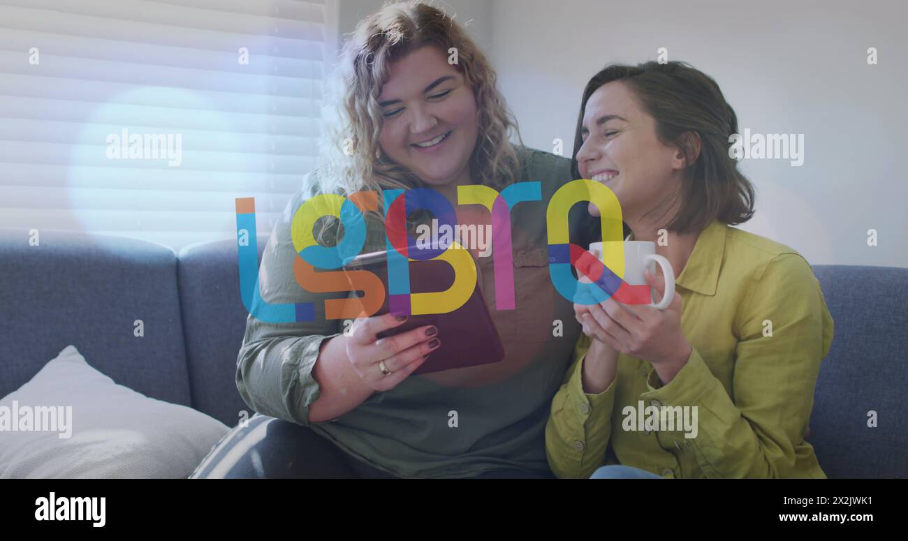 Image of lgbtq over happy caucasian lesbian couple using tablet and sitting on sofa at home Stock Photo