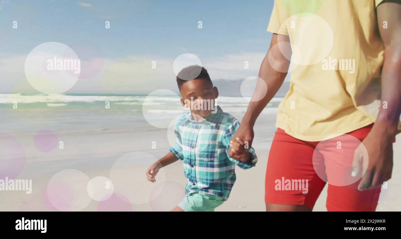 Image of light spots over happy african american father and son walking on beach Stock Photo