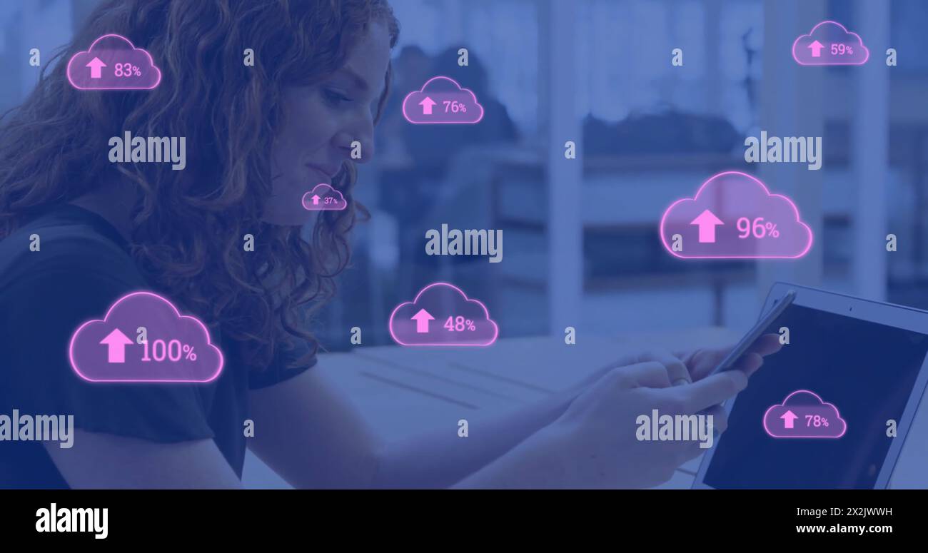 Image of pink clouds uploading data over caucasian businesswoman using smartphone and laptop Stock Photo