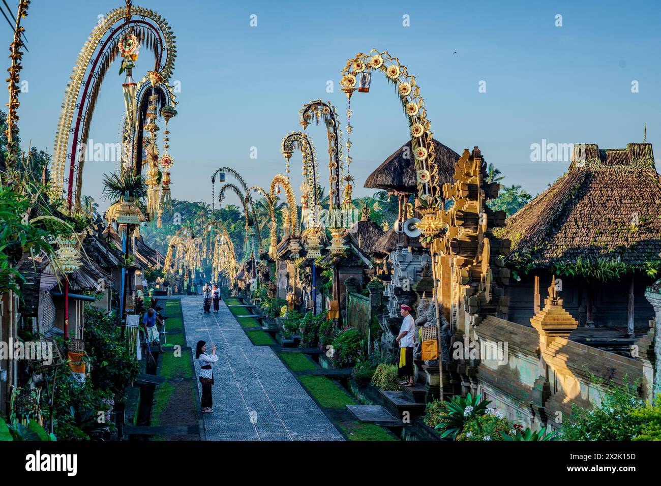 Morning view of a beautifully decorated traditional village in Bali, Indonesia, with festive bamboo poles and locals walking. Stock Photo