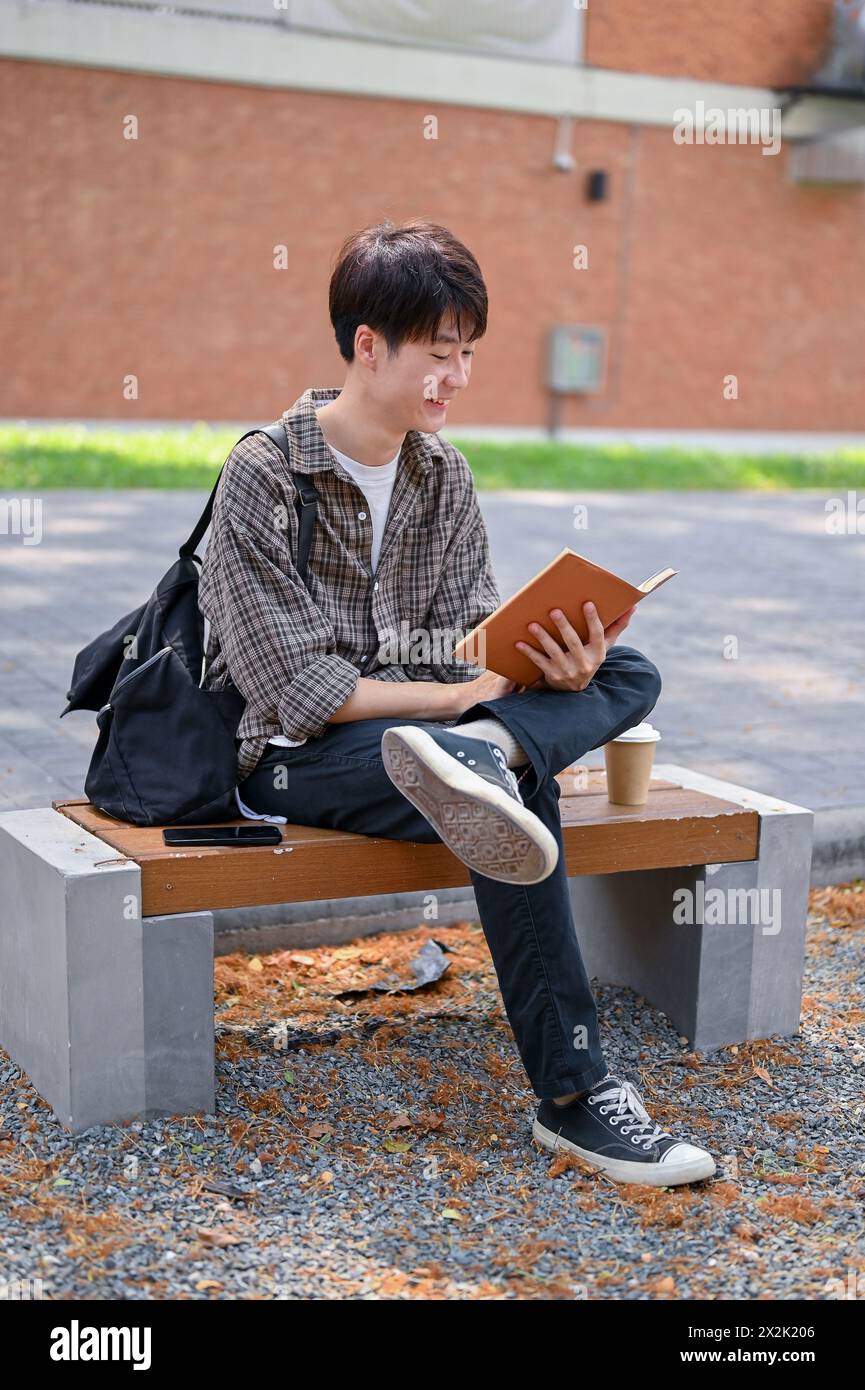 A happy, relaxed young Asian male college student sits on a bench in ...