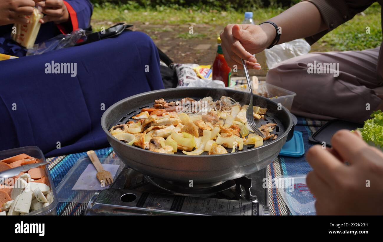 Grill sausages, meatballs and other food ingredients using a portable stove when picnicking with friends in the morning Stock Photo