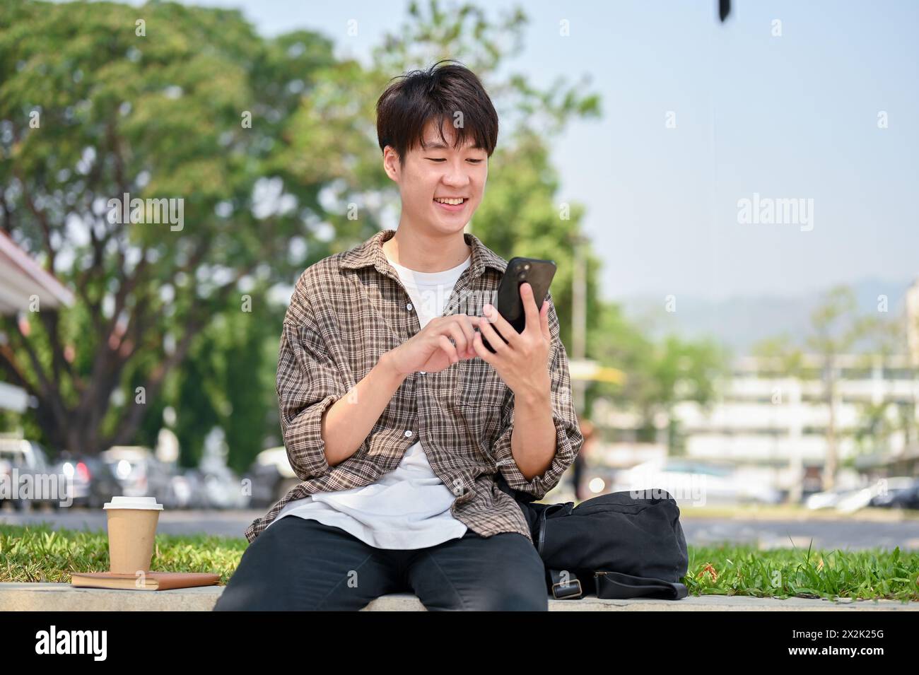 A cheerful young Asian male college student in casual wear sits on a ...