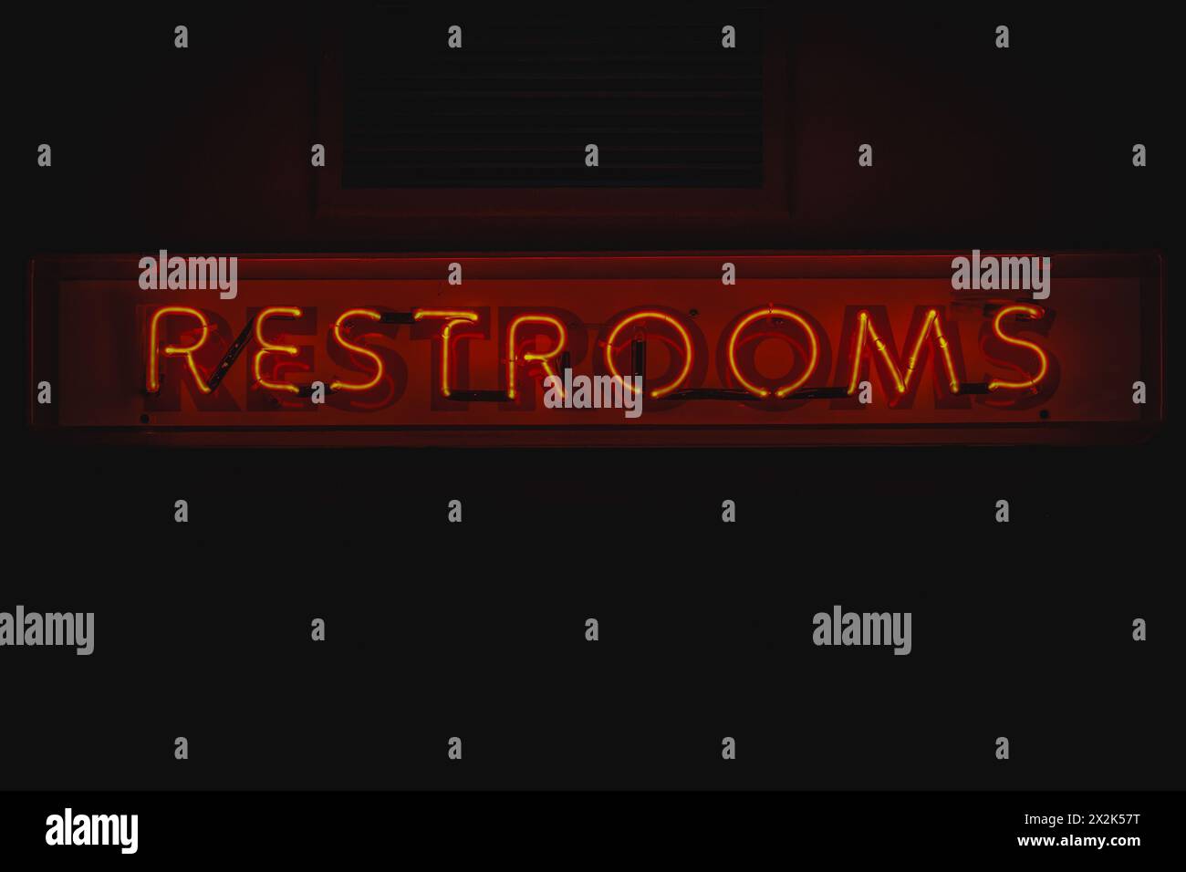 A vibrant red neon sign displaying the word 'RESTROOMS' mounted on a dark wall, emitting a soft glowing light in a dimly lit ambiance. Stock Photo