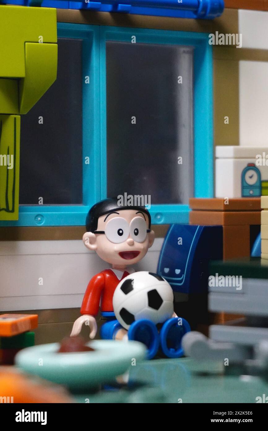 The Japanese toy figure is Nobita who is sitting and leaning against the wall while holding a ball Stock Photo