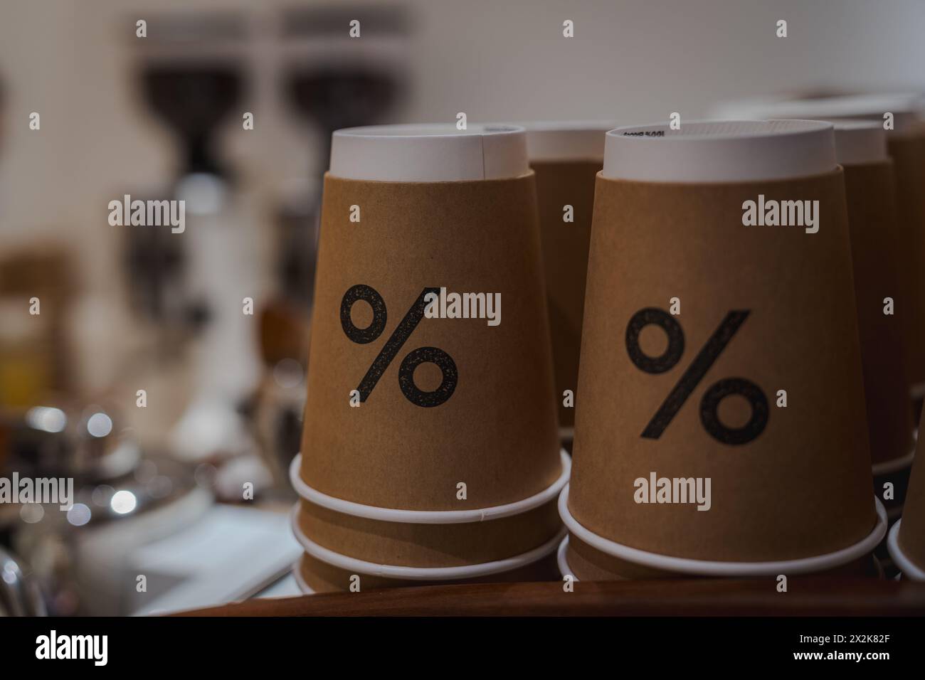 Eco-friendly paper coffee cups with a bold percent sign, showcased on a cafe counter against a blurred background. Arabica cafe percentage Stock Photo