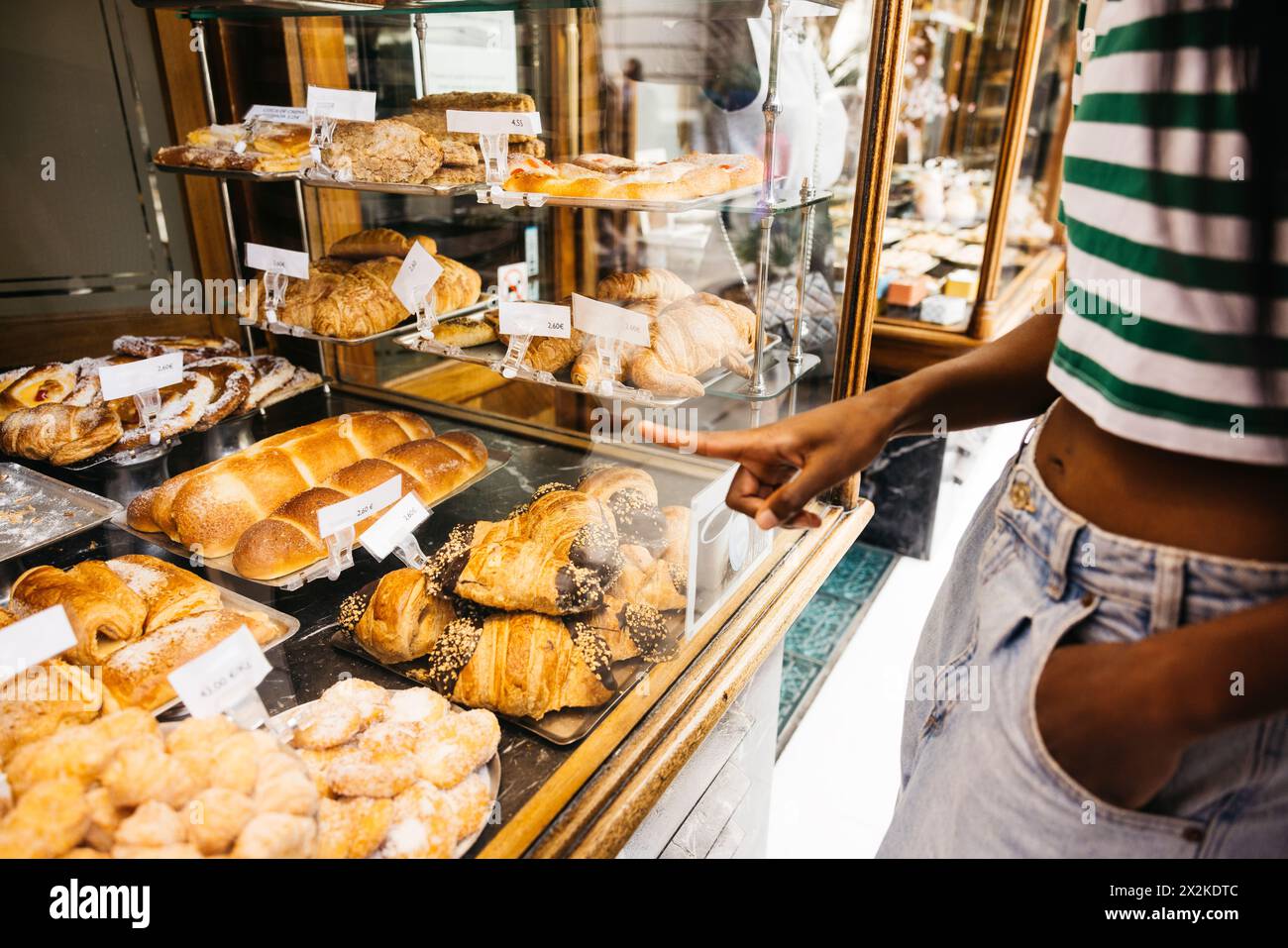 Young black woman gazing at the window display of a pastry shop and pointing with her finger the sweet she deserves. Stock Photo