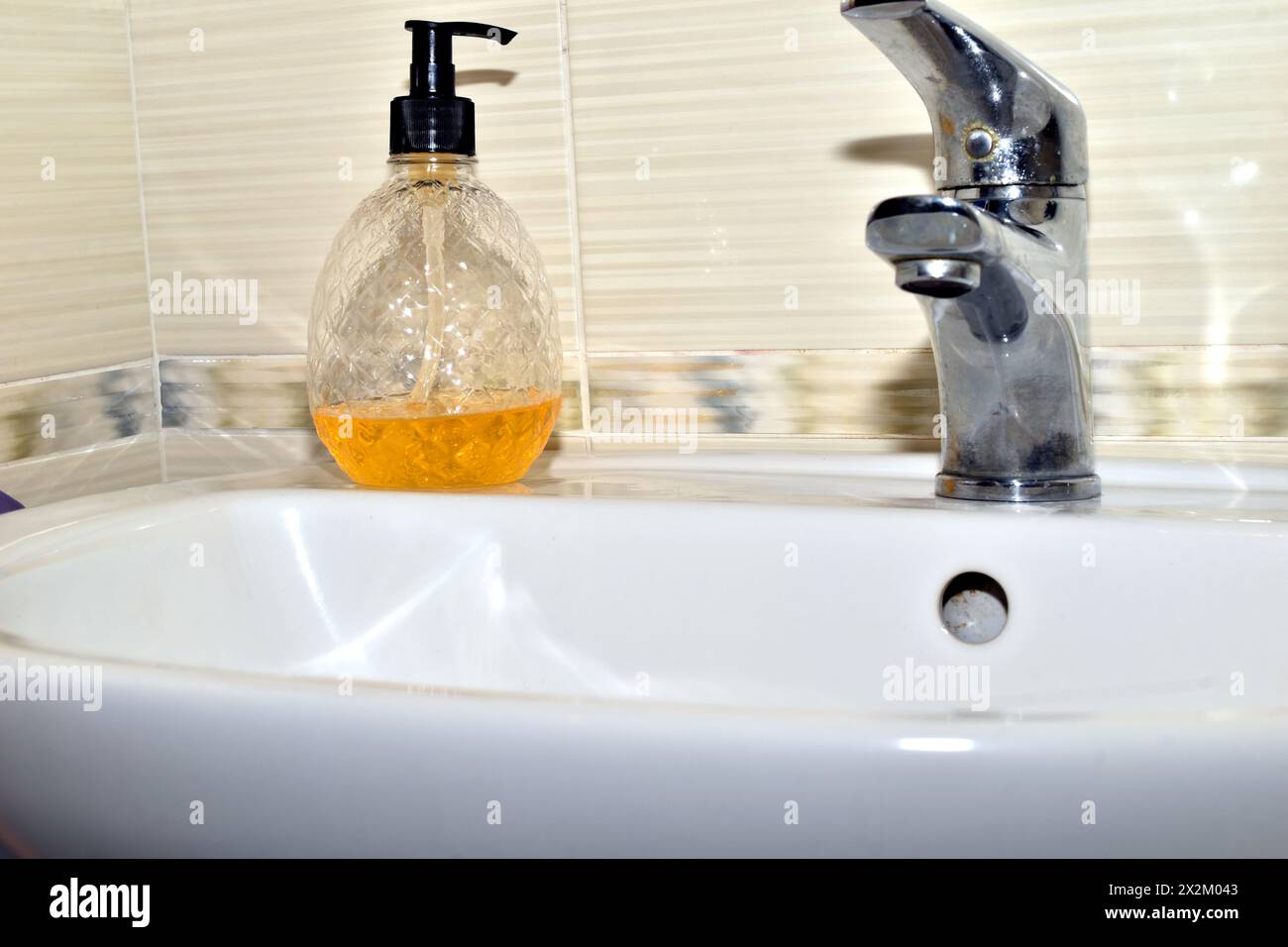 On the washbasin in the bathroom there is a bottle of yellow liquid soap. Stock Photo