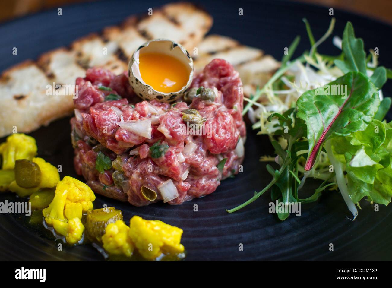 Steak tartare with quail egg, toast and piccalilli on plate in a restaurant Stock Photo