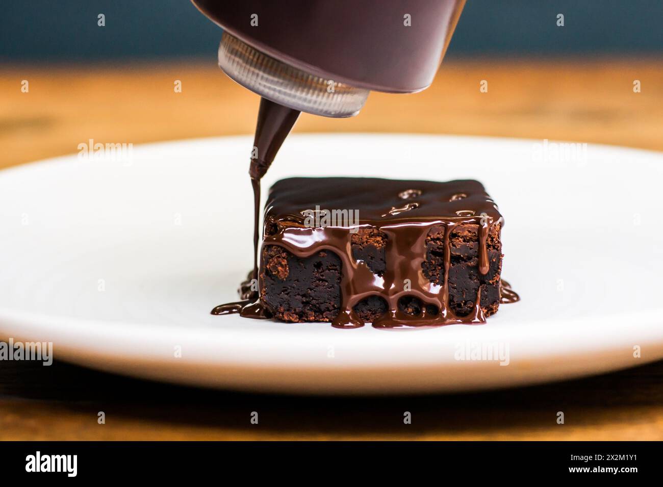 Chocolate sauce being poured onto brownie on white plate on wooden restaurant table Stock Photo