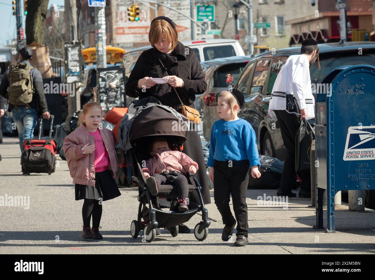 A street scene in a Jewish neighborhood in Brooklyn where a mother & her children stop as she reads what appears to be an instruction sheet. Stock Photo