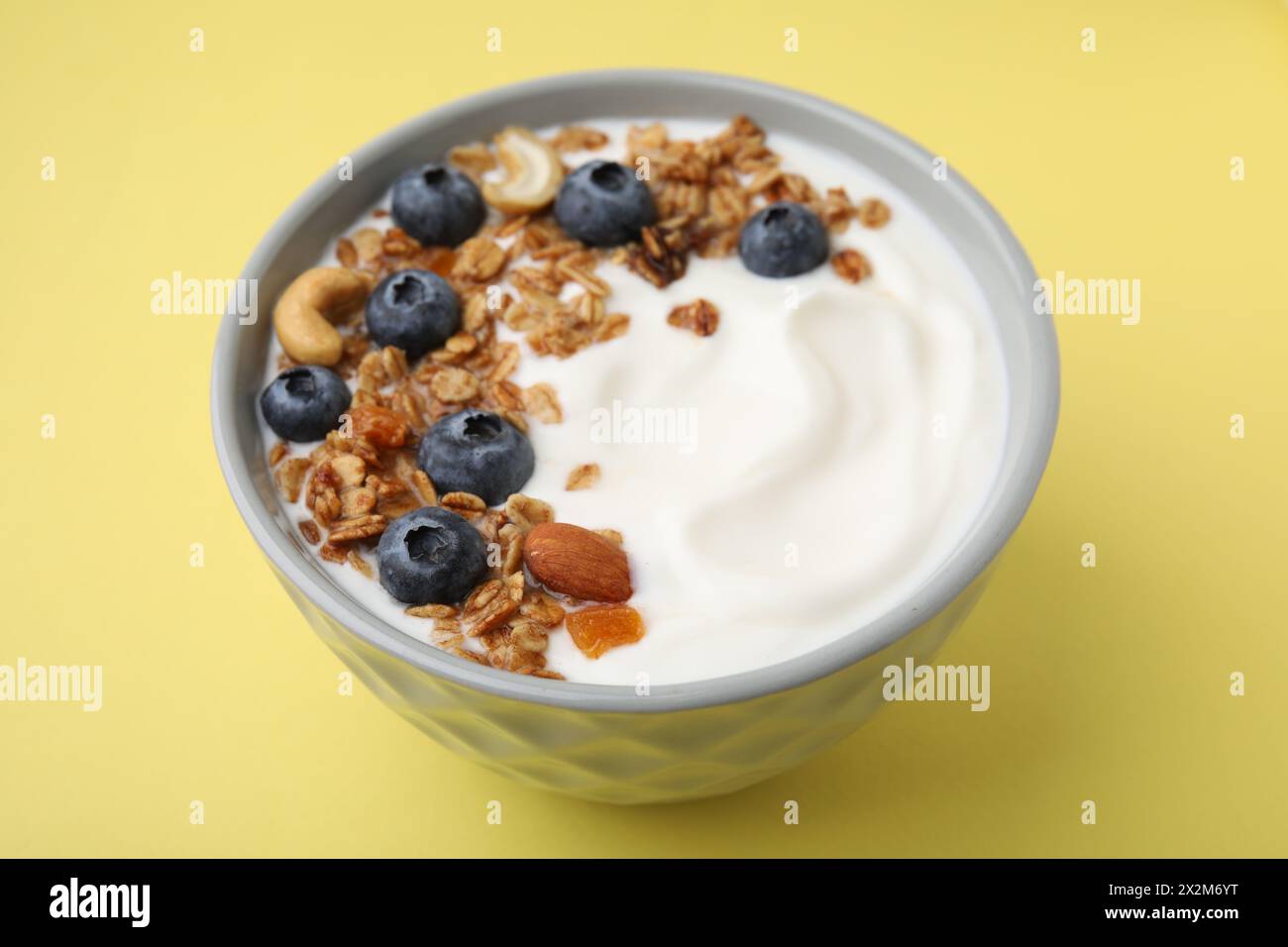 Bowl with yogurt, blueberries and granola on yellow background, closeup Stock Photo