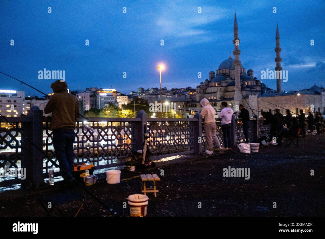 Fishermen on the Galata Bridge on the estuary of the Golden Horn at dusk, linking the districts of Sultanahmet and Galata, with the New Mosque (Yeni C Stock Photo