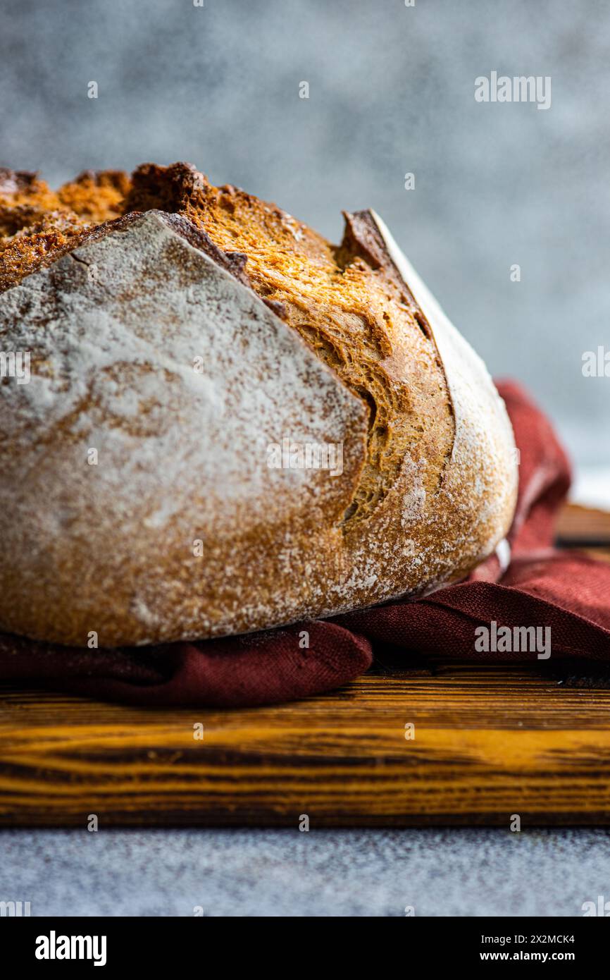 A close-up of a crusty artisan sourdough loaf made with wholesome rye flour, resting on a rustic wooden board with a burgundy cloth Stock Photo