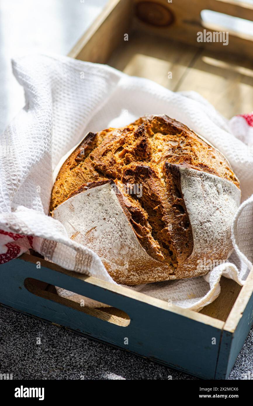 A fresh loaf of artisanal sourdough bread made from rye flour, presented in a wooden tray with a linen cloth, showcasing a rustic kitchen theme Stock Photo