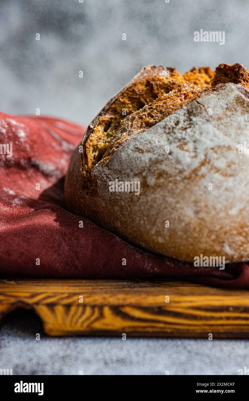 Artisanal sourdough bread made with rye flour, displayed on a wooden cutting board with a red cloth backdrop Stock Photo
