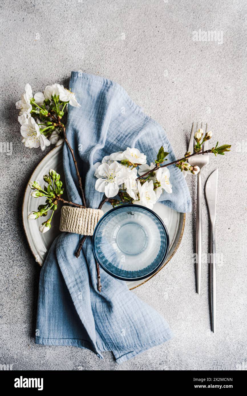 A serene table setting themed with cherry blossoms, featuring a ceramic plate, blue napkin, and delicate spring flowers Stock Photo