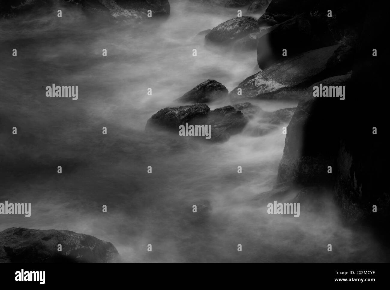 Black and white photography captures the serene motion of mist-like water meandering around coarse rocks. Stock Photo