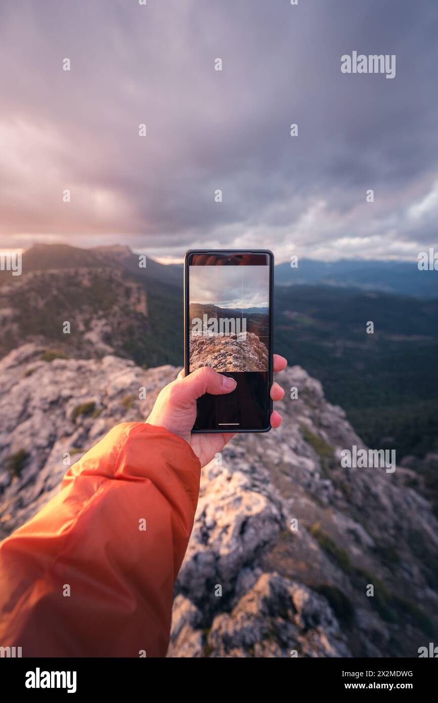 A person's hand holding a smartphone that captures a stunning mountainous landscape, symbolizing the fusion of technology and nature at the breathtaki Stock Photo