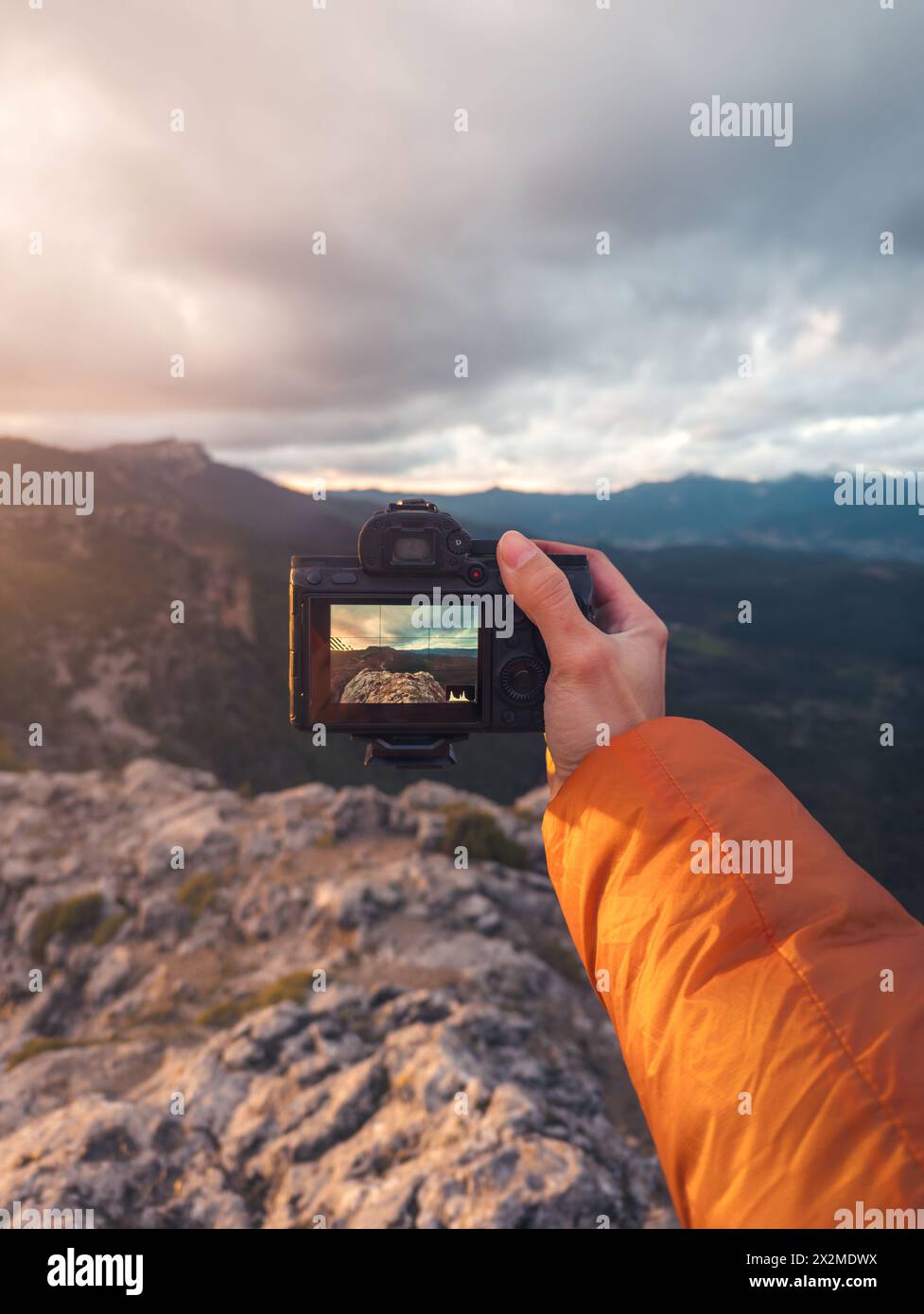 A person's hand holding a camera that captures a stunning mountainous landscape, symbolizing the fusion of technology and nature at the breathtaking o Stock Photo