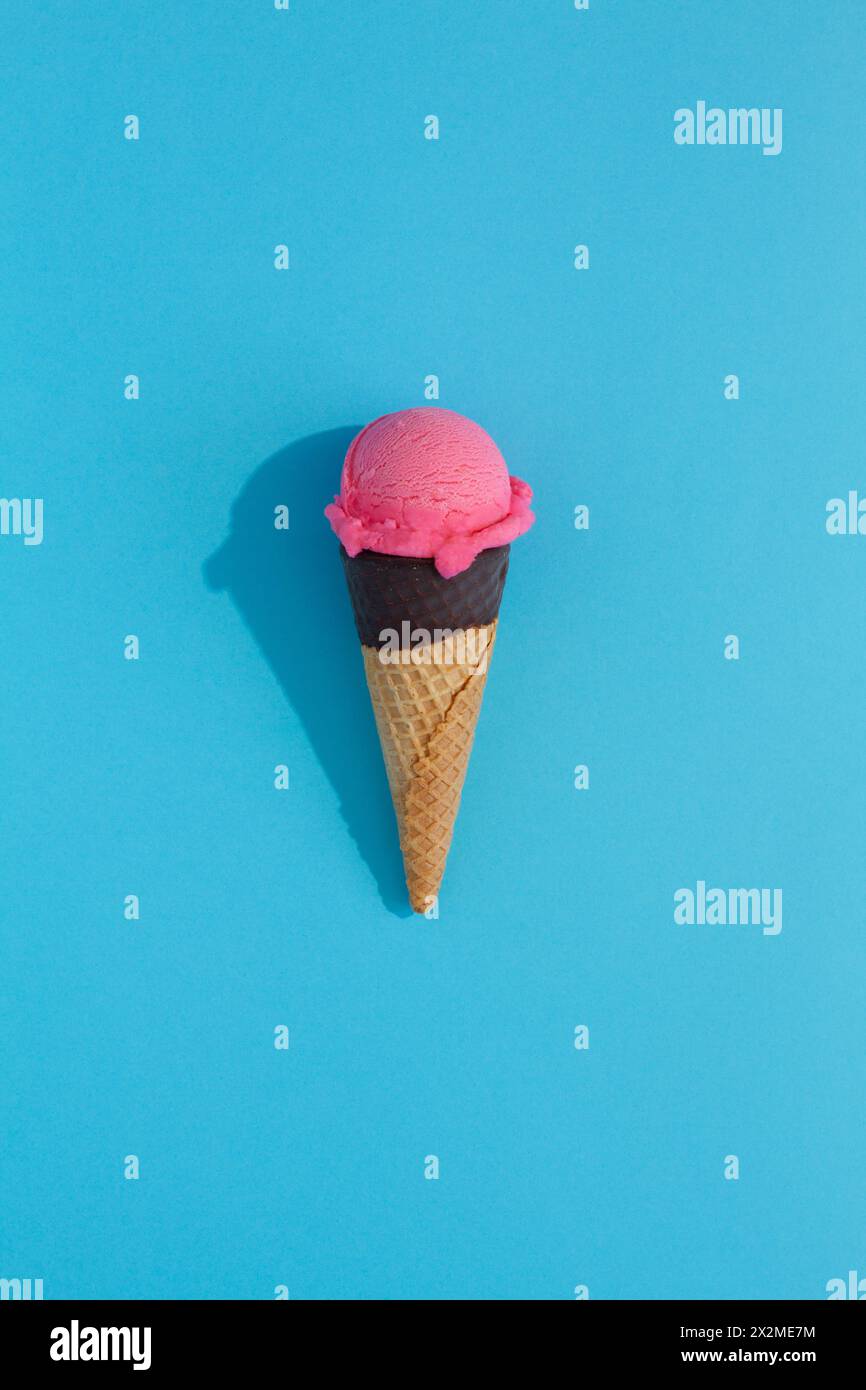 A vibrant Strawberry ice cream scoop sits atop a classic waffle cone against a blue background, casting a playful shadow Stock Photo