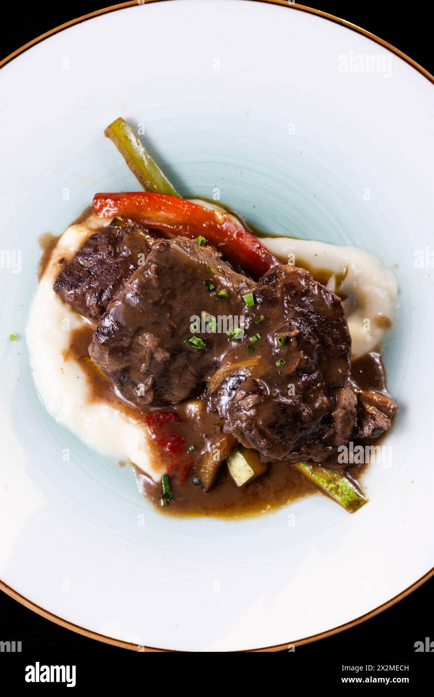 Top view of tantalizing pork cheeks paired with a rich Pedro Ximenez reduction, elegantly presented on a creamy mashed potato base surrounded by saute Stock Photo