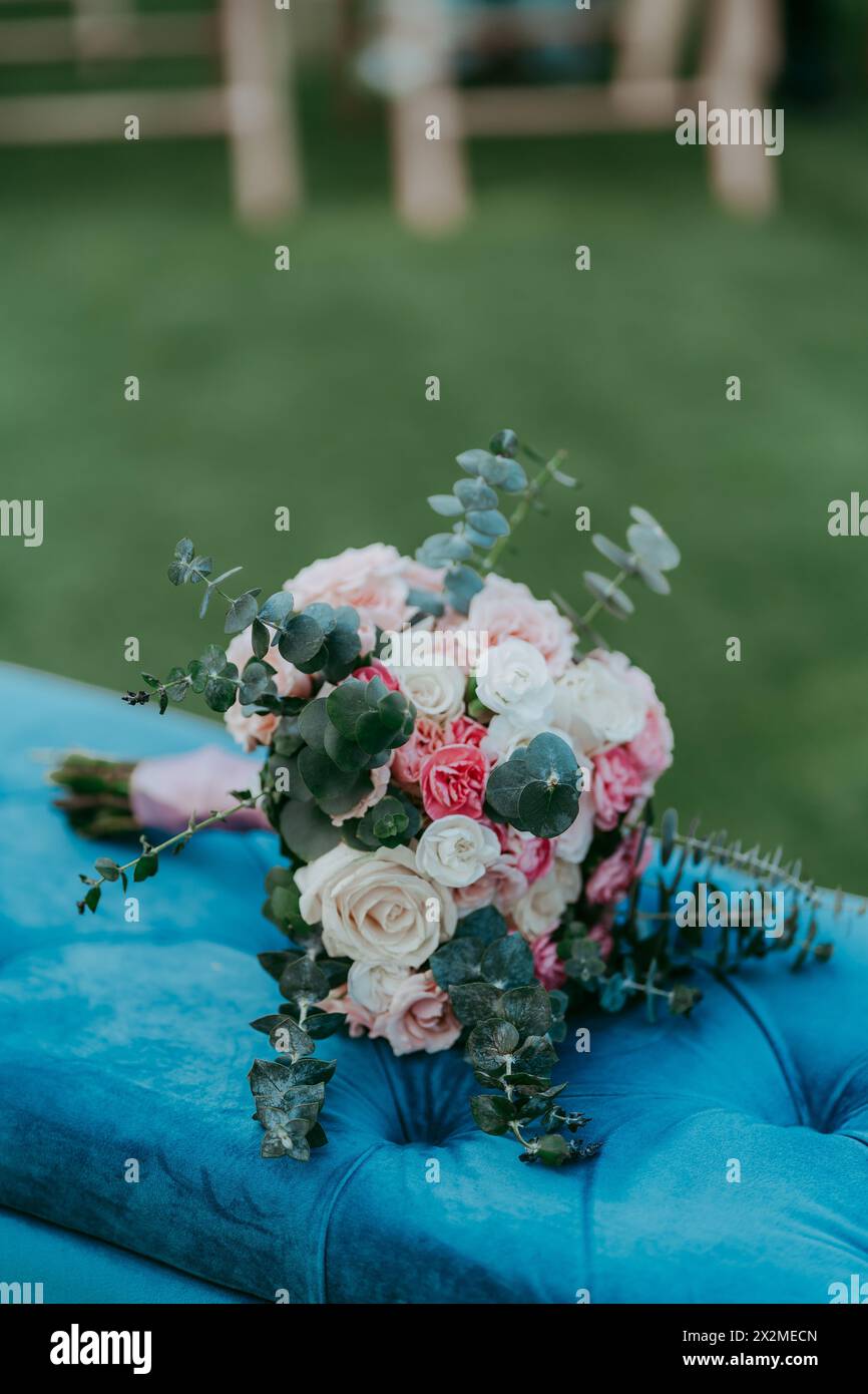 Elegant bridal bouquet with a mix of roses and greenery, placed on a blue velvet chair Stock Photo