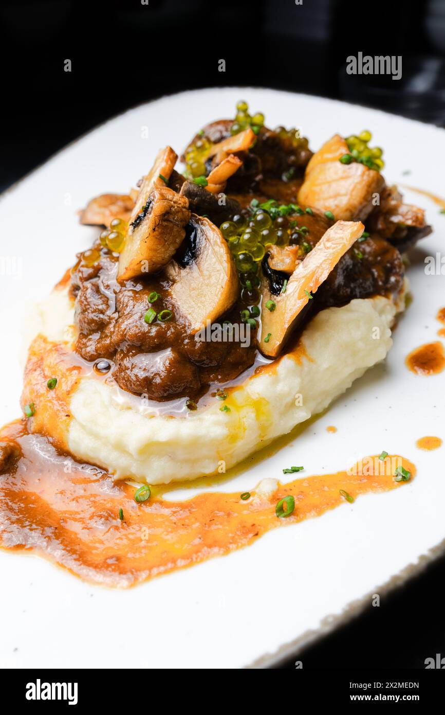 Succulent pork cheeks cooked in Pedro Ximene reduction, served over creamy mashed potatoes, garnished with mushrooms and chives. Stock Photo