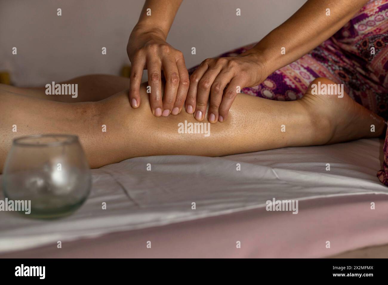 Latina woman lying on her back receives an ayurvedic massage treatment on her calf, foreground hands of a woman masseuse. Healing massage concept Stock Photo