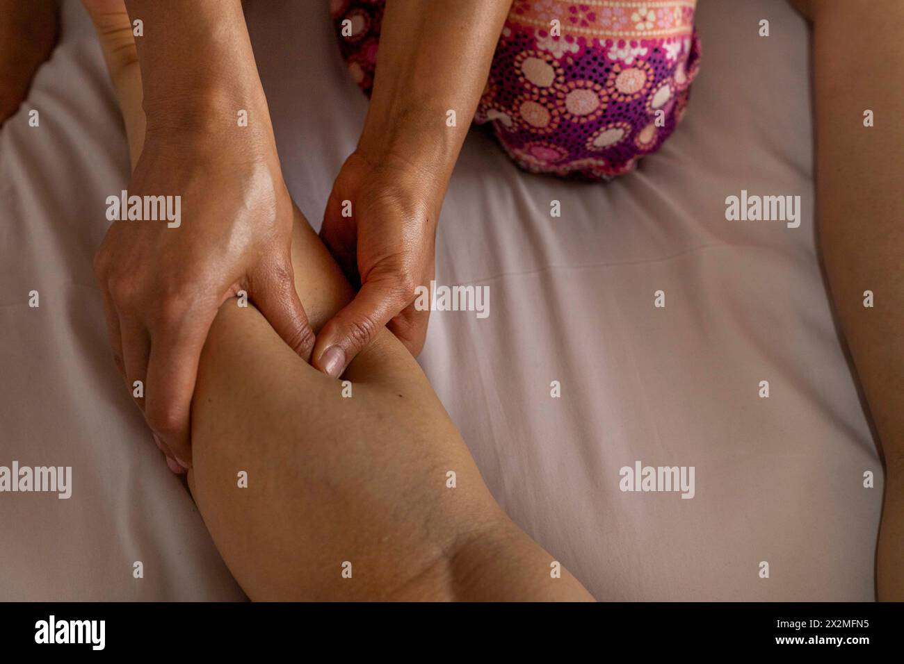 Latina woman lying on her back receives an ayurvedic massage treatment on her calf, foreground hands of a woman masseuse. Healing massage concept Stock Photo