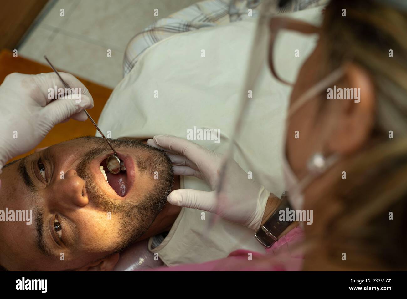 Latin American adult male (42) is examined by a female dentist using a dental mirror. zenithal view. Concept of health and dentistry. Stock Photo