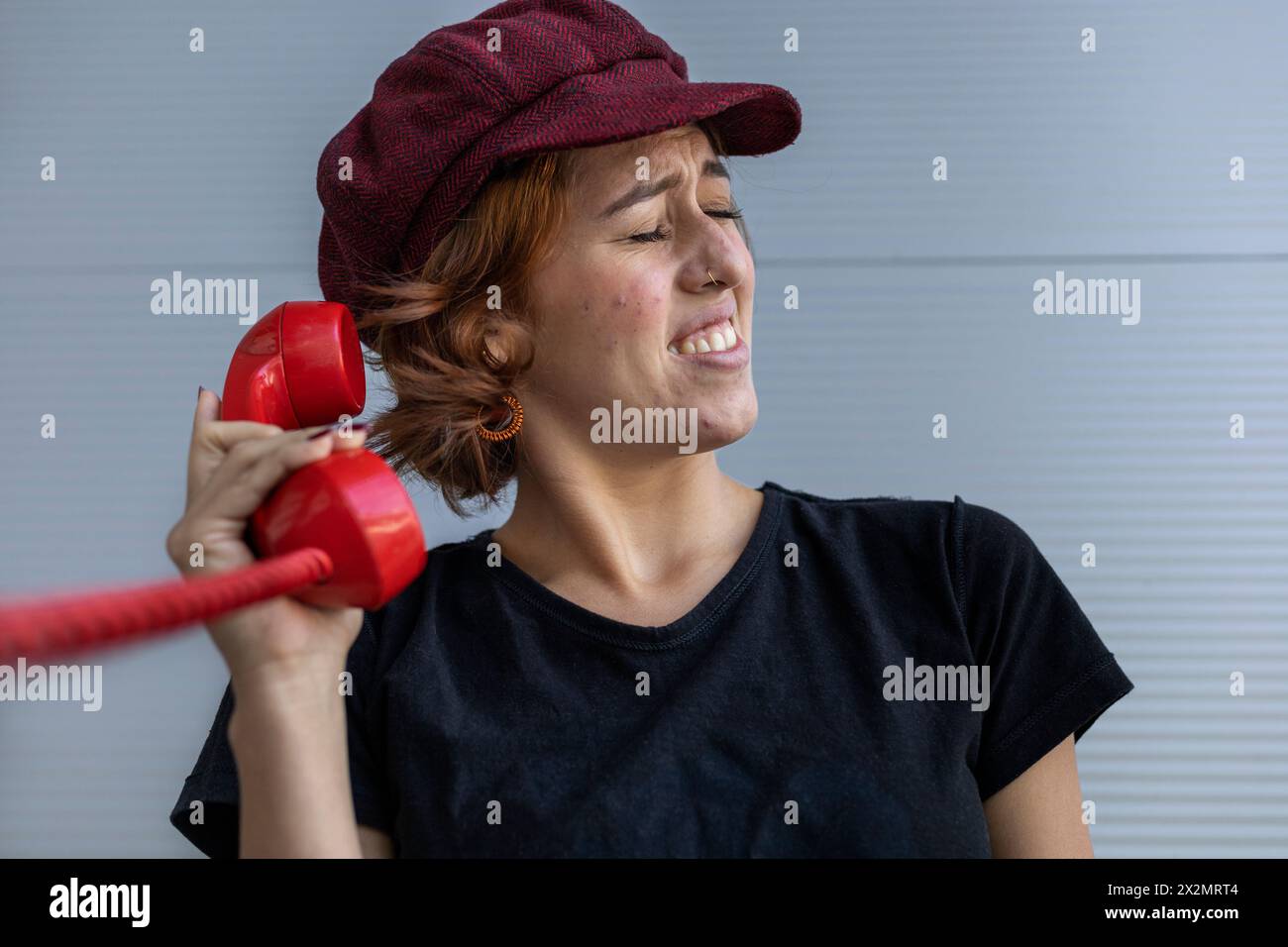 Medium short shot of Latin American young woman (22) with cap and red hair uncomfortable because of the screams she hears from the conversation over t Stock Photo