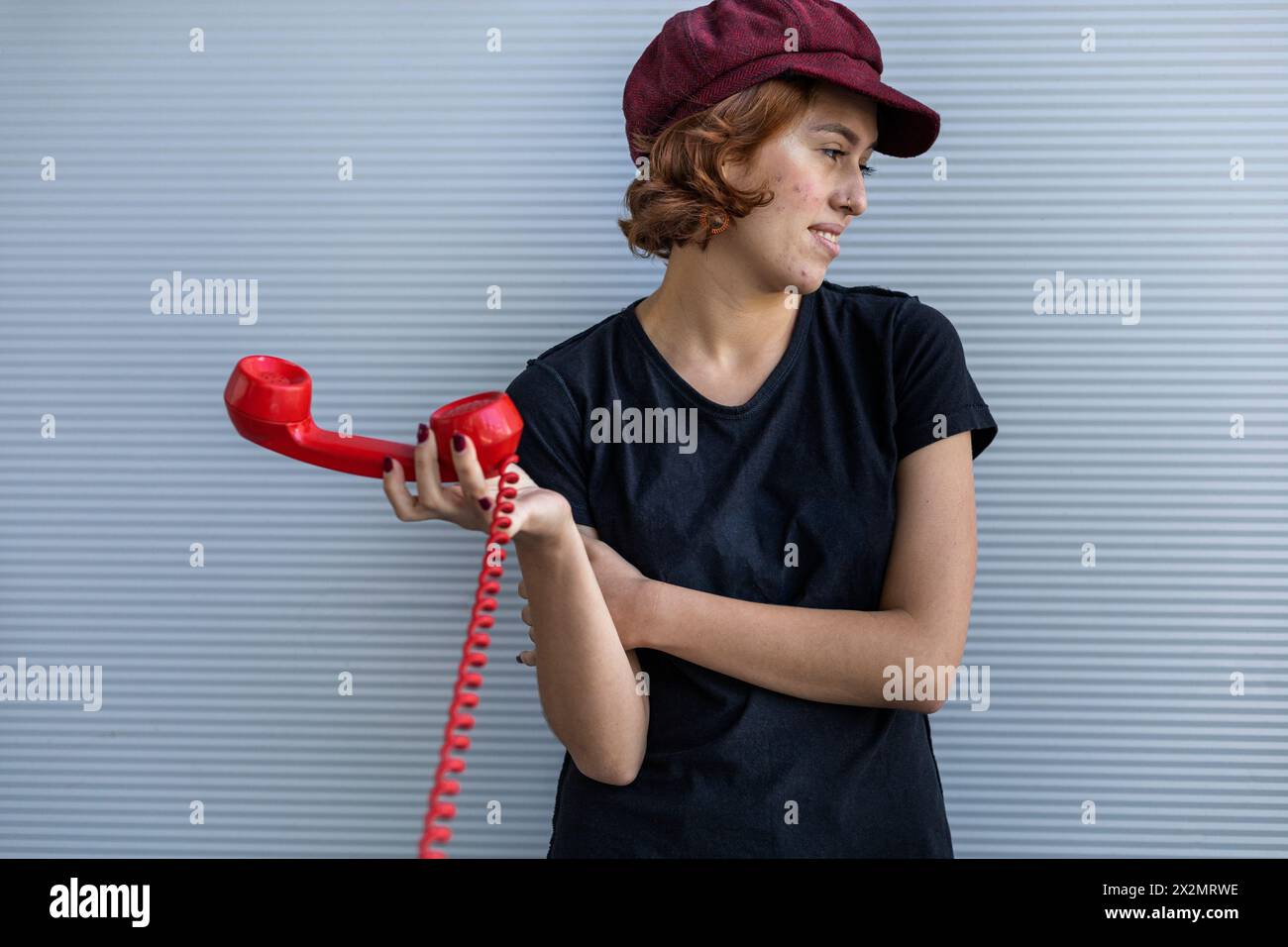 Medium short shot of Young Latin American woman (22) with cap and red hair, not interested in conversation and puts away the handset of her retro Hand Stock Photo