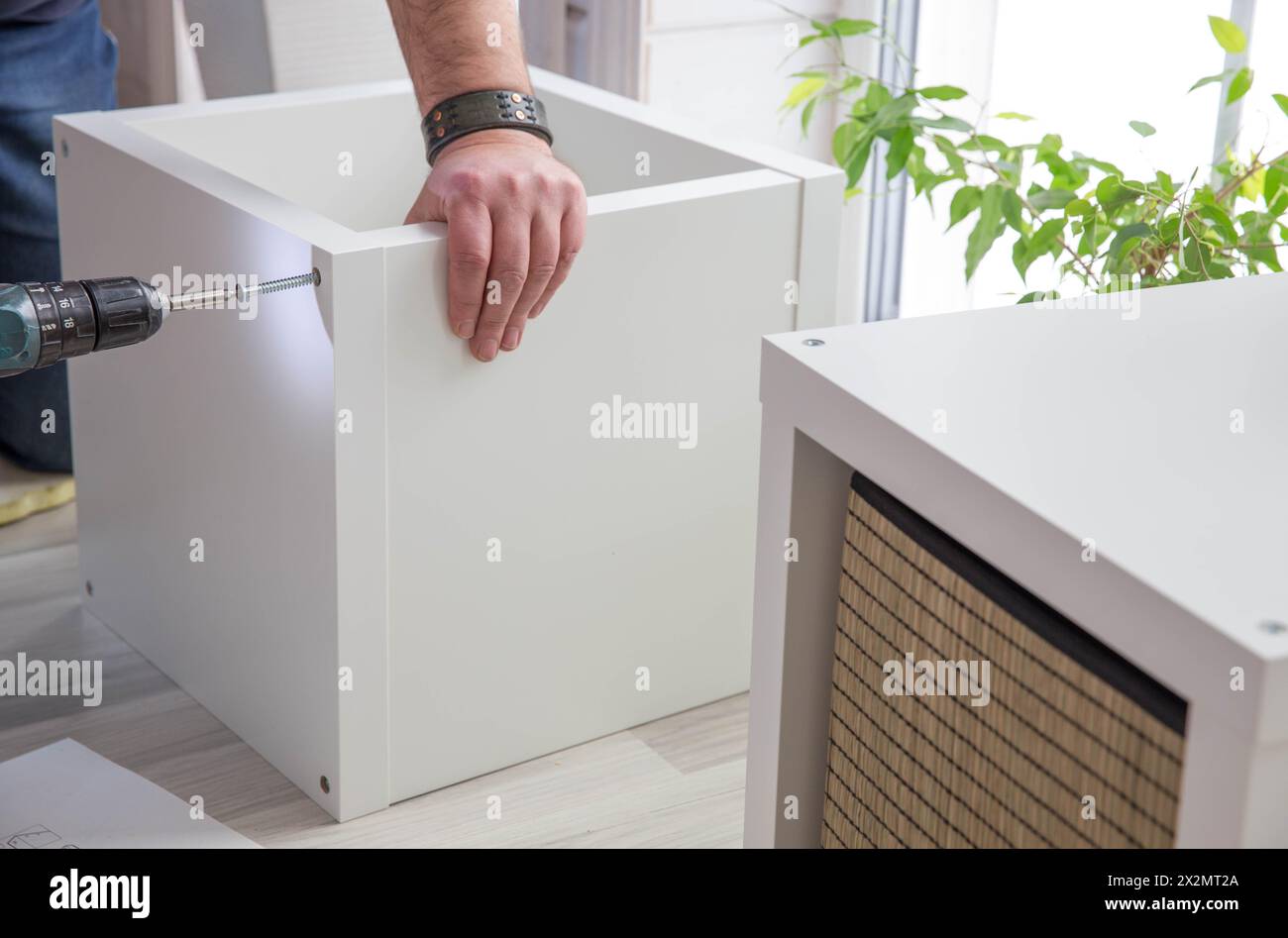 Man assembling purchased furniture in room with window. Concept DIY or furniture assembly services Stock Photo