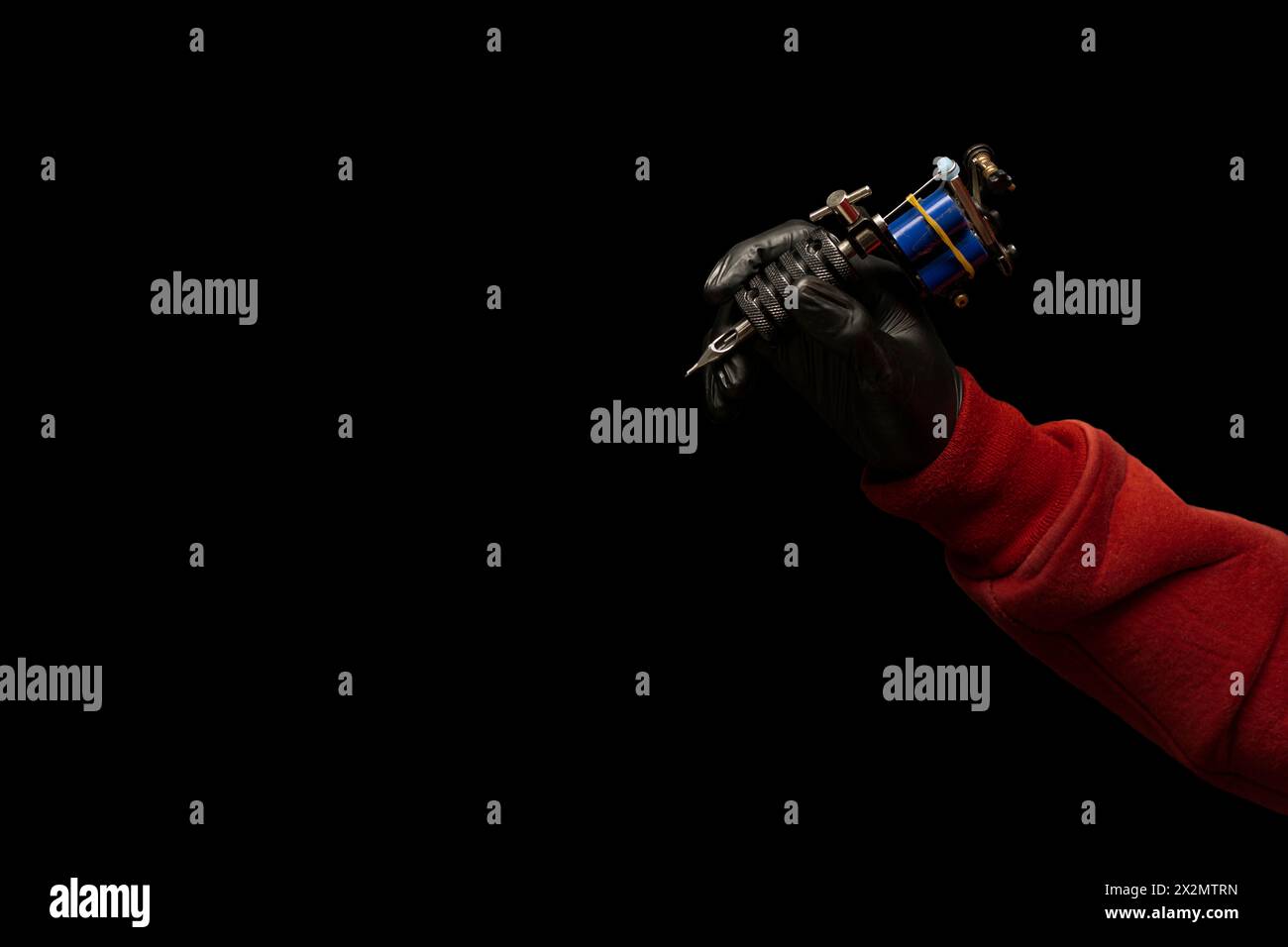 Right arm with red sweater sleeve extended while holding in his black gloved hand a tattoo machine, black background copy space. Body art concept Stock Photo
