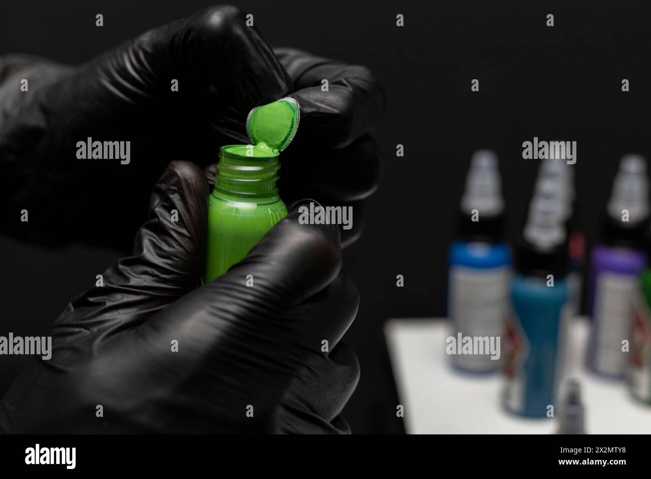 Uncapping a bottle of green tattoo ink, background of bottles of different inks and work table. Body art concept Stock Photo