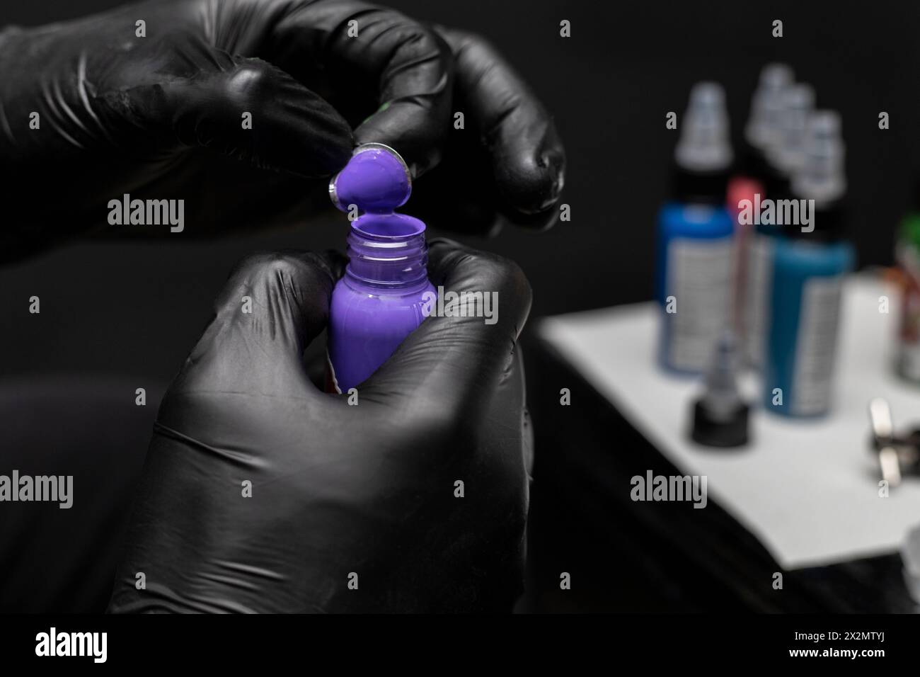 Uncapping a bottle of purple tattoo ink, background of bottles of different inks and work table. Body art concept Stock Photo