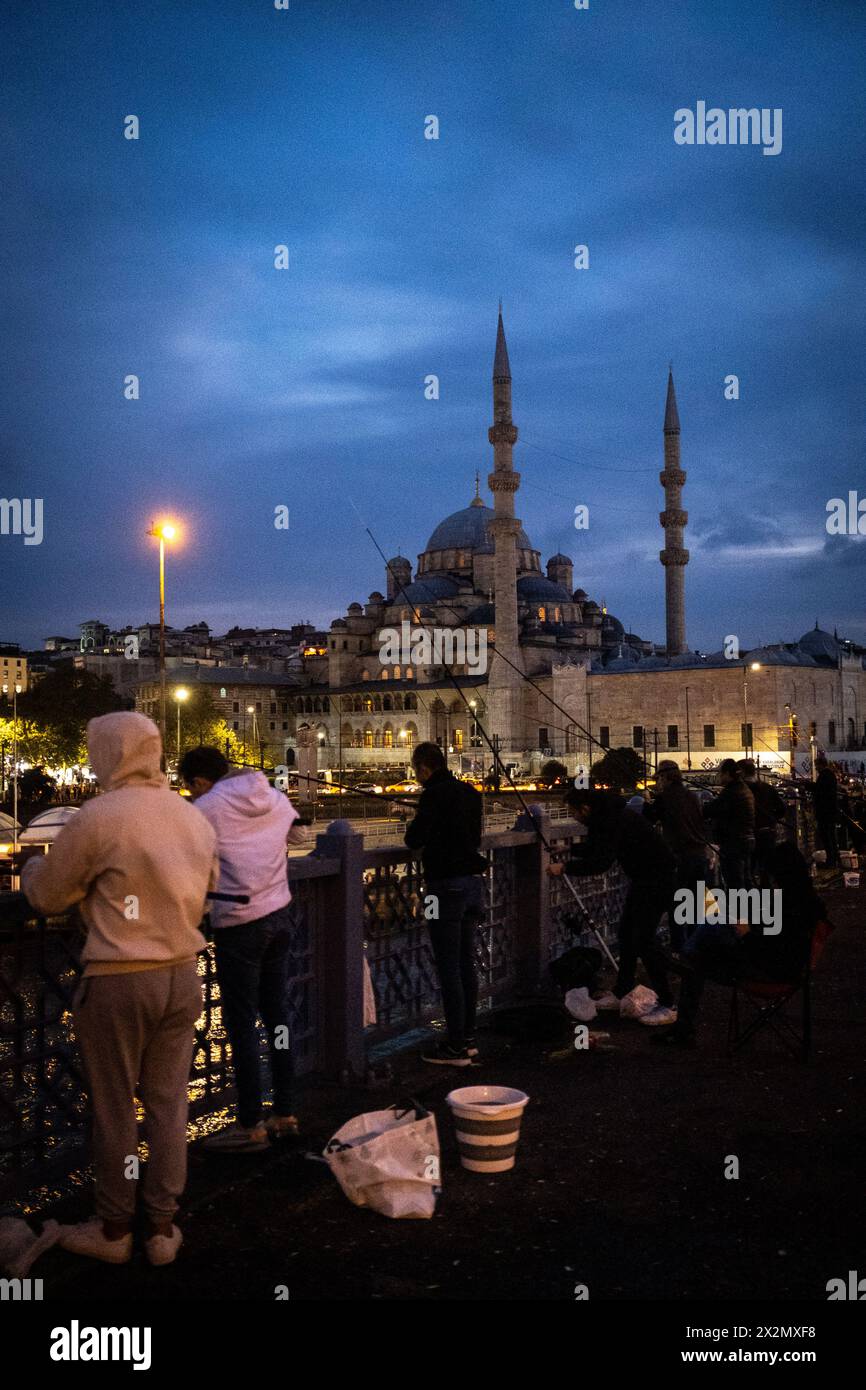 Fishermen on the Galata Bridge on the estuary of the Golden Horn at dusk, linking the districts of Sultanahmet and Galata, with the New Mosque (Yeni C Stock Photo