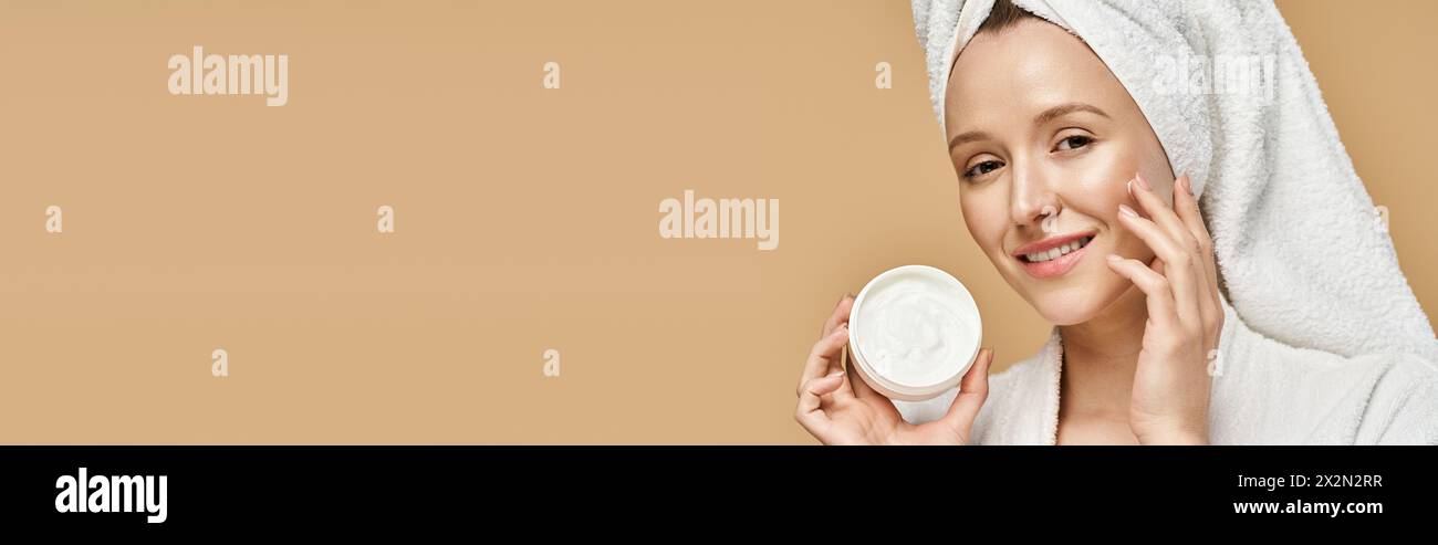 An attractive woman with a towel on her head actively holding a jar of cream. Stock Photo