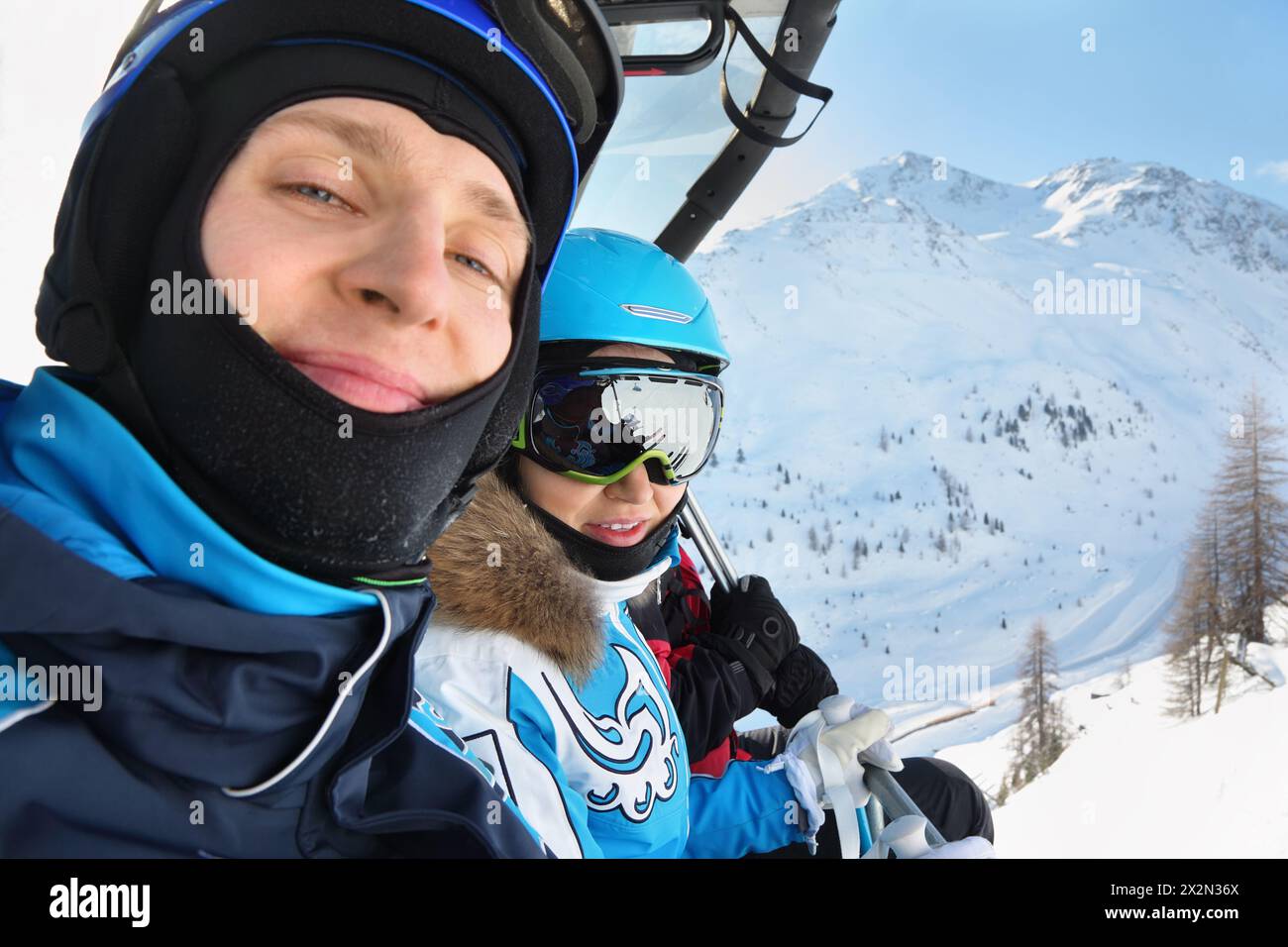 Male and female skiers in special clothing ride on cable car in mountains. Focus on woman. Stock Photo