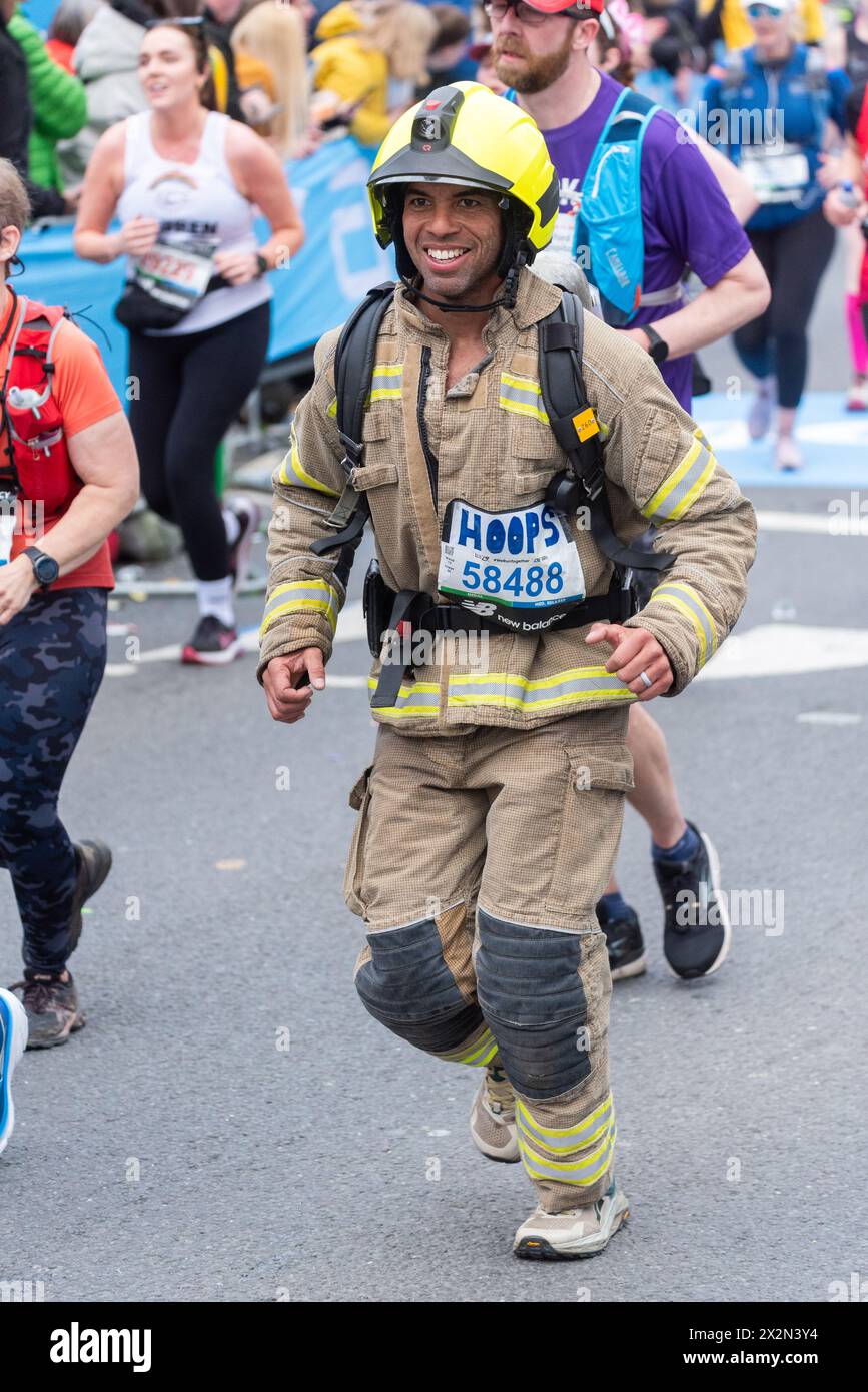Matt Hooper participating in the TCS London Marathon 2024 passing through Tower Hill, London, UK, running in firefighter uniform Stock Photo