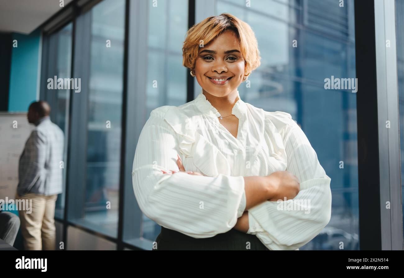 Happy and successful black businesswoman stands in a boardroom office. She has her arms crossed, smiling and looking directly at the camera. With a pr Stock Photo